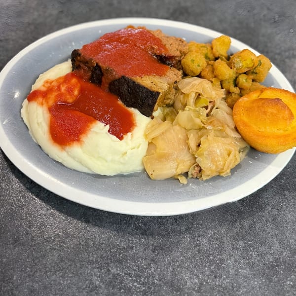 Southern meatloaf with mashed potatoes, fried okra, cabbage, and a cornbread muffin on a plate.