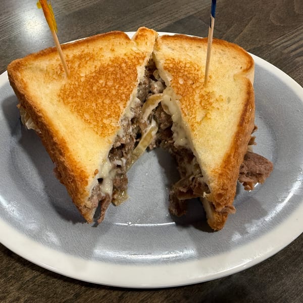 A Southern Spice cheesesteak sandwich, cut in half, revealing melted cheese and steak, on a gray plate.